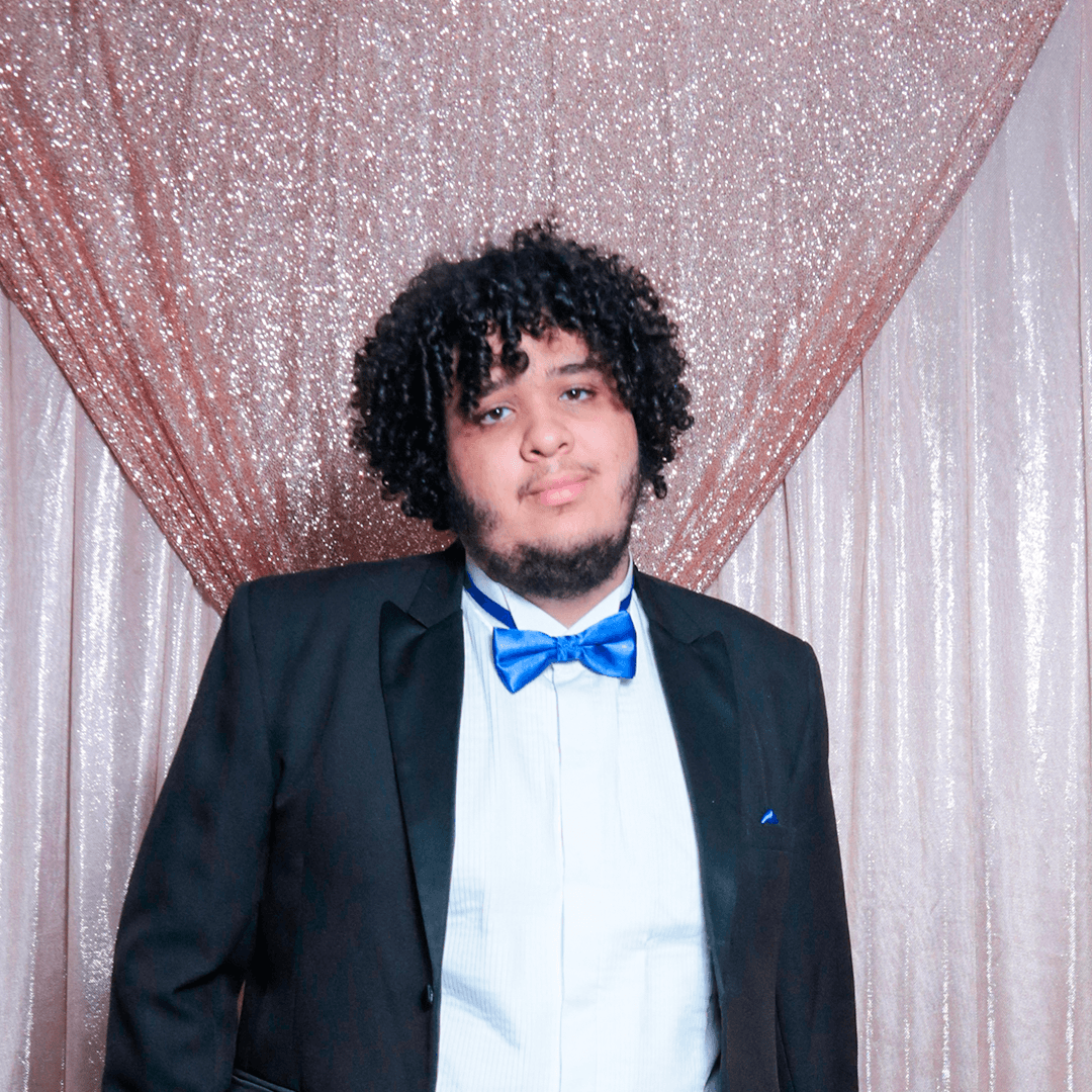 chubby boy in a dark blue smoking with blue decorations holding a sign in front of himself